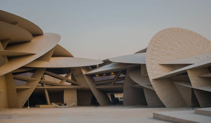 The National Museum of Qatar (NMoQ) is an architectural masterpiece that blends history, culture, and modern design. Opened to the public on March 28, 2019, the museum was designed by the French architect Jean Nouvel, the same mind behind iconic structures like the Louvre Abu Dhabi.

Architectural Inspiration
Nouvel’s design is inspired by the desert rose, a natural crystalline formation found in Qatar’s arid landscape. The building consists of a complex interlocking structure made up of 539 massive disc-shaped panels, mimicking the layered petals of a desert rose. These discs aren’t just for aesthetics—they provide shade, regulate heat, and reduce glare, making the museum well-suited for Qatar’s harsh climate. The entire structure is built around the restored Old Palace of Sheikh Abdullah bin Jassim Al Thani, which was once Qatar’s royal residence and seat of government.

Construction & Challenges
The project took over a decade to complete due to its sheer complexity. Engineers had to create custom-made joints and support structures to connect the irregularly shaped discs while ensuring structural stability. The exterior is made of glass fiber-reinforced concrete, which gives it a seamless, natural look while being durable enough to withstand the desert environment.

Cultural & Historical Significance
The museum’s exhibits take visitors on a journey through Qatar’s past, present, and future, covering topics like Bedouin traditions, maritime history, oil discovery, and modernization. It houses interactive installations, artifacts, and immersive storytelling experiences to bring Qatar’s heritage to life.

Jean Nouvel himself described the museum as a place where visitors don’t just see history but "experience it as if they are walking through time.” It’s not just a museum—it’s a symbol of Qatar’s identity, blending its deep-rooted history with its vision for the future.

Wouldn’t be surprised if people mistake this place for a set in a sci-fi film!